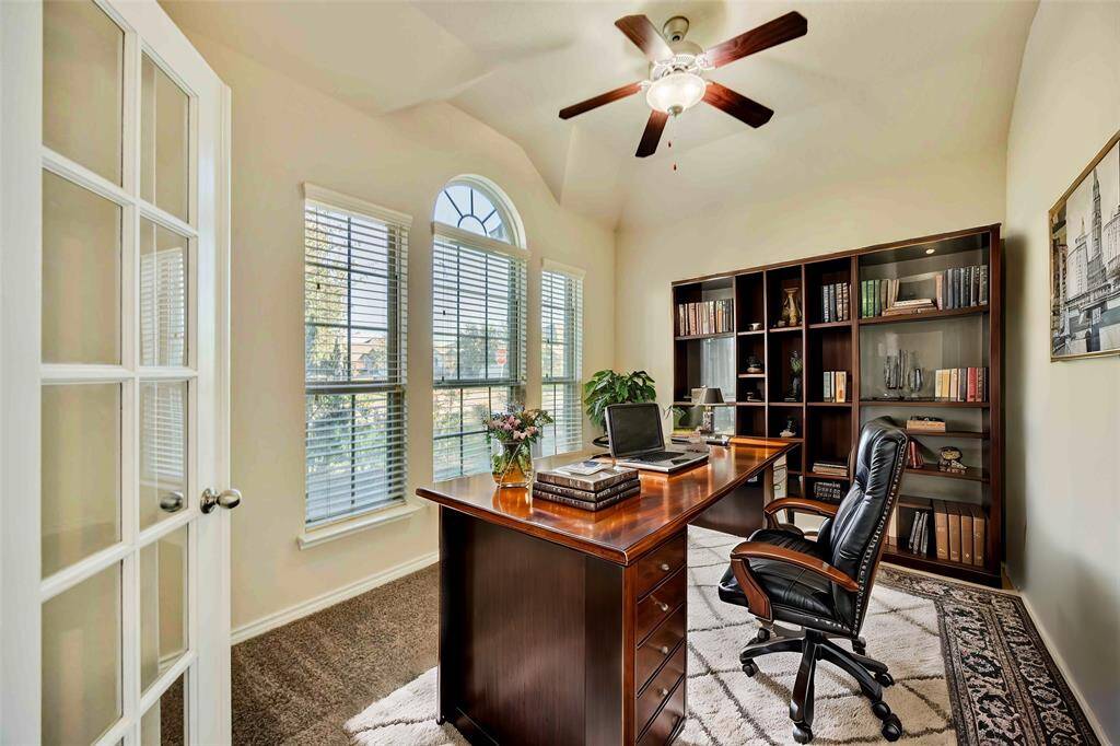 This bright, airy home office features large windows, elegant French doors, and a ceiling fan. It's a perfect atmosphere for working from home.