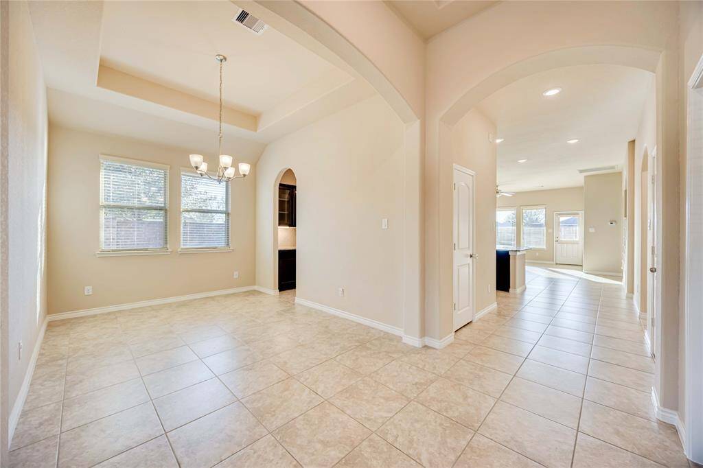 This spacious home features an open floor plan with elegant arches, plenty of natural light, and neutral tile flooring. The dining area is enhanced by a modern chandelier, and there's easy access to a bright living space with large windows.