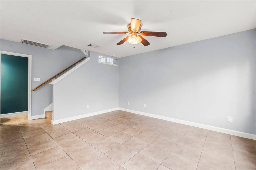 This photo showcases a bright and open kitchen-living area with tile flooring. The kitchen features modern appliances, white cabinetry, and a central island with a sink. A stylish chandelier and ceiling fan add elegance and comfort. The space is perfect for entertaining or family gatherings.