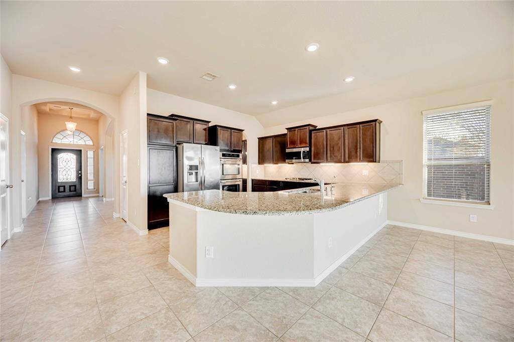 This spacious kitchen features elegant dark wood cabinets, granite countertops, and stainless steel appliances. The open layout includes a large island with a sink, perfect for entertaining.