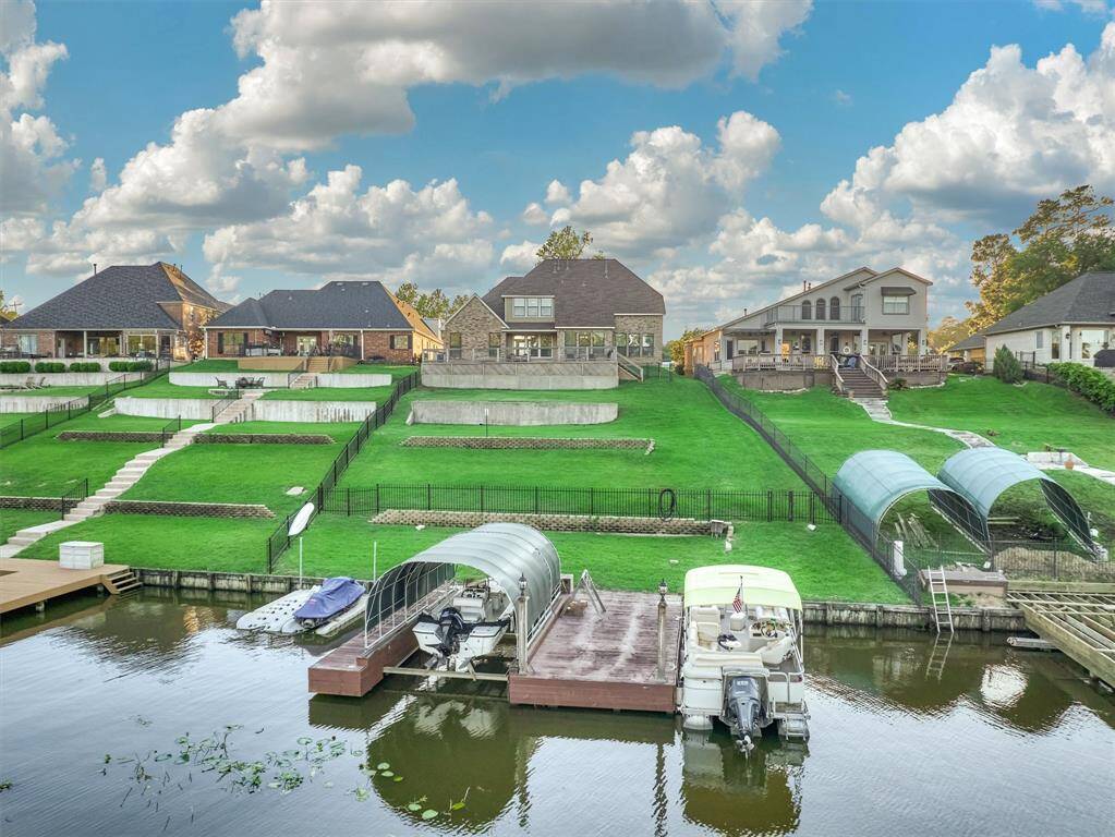 This property features a covered boat slip with lift, two floating jet ski lifts, and a private fishing pier—perfect for enjoying lake life to the fullest. A wrought iron fence encloses the yard.
