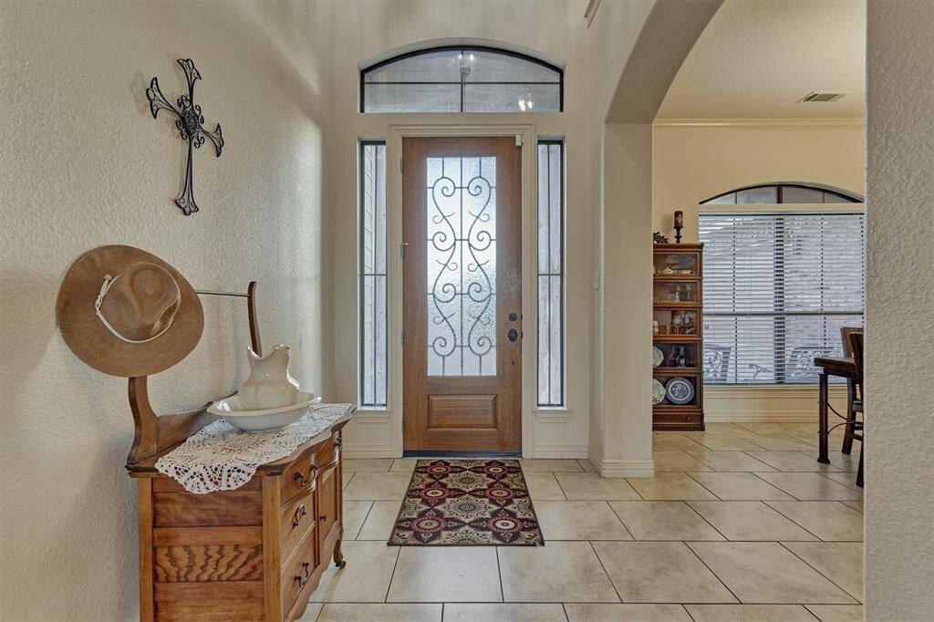 The wood-stained front door features elegant iron accents, flanked by sidelights and topped with transom windows to fill the entry with natural light.