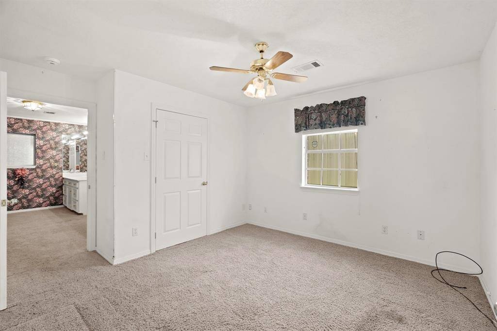 This bright bedroom features neutral carpeting, a ceiling fan, and a window with floral valance. It connects to the primary bathroom and bedroom which makes for great use for an office or a child nursery.
