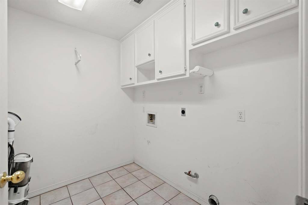 This photo shows a laundry room with tiled flooring, white walls, and built-in overhead cabinets. It includes hookups for a washer and dryer.