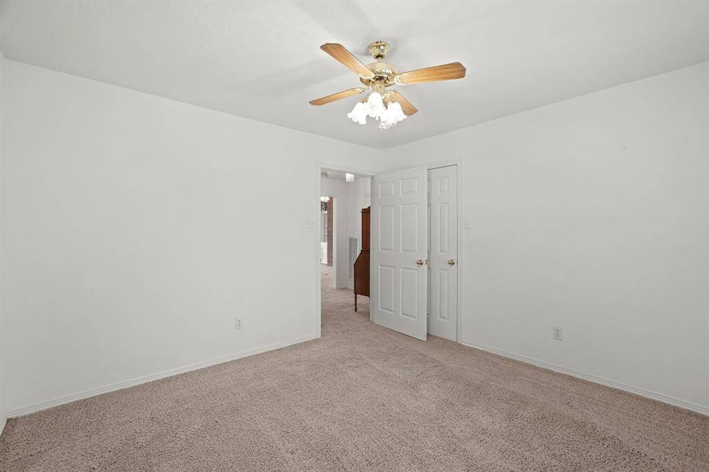 This photo shows a bright, carpeted bedroom with white walls and a ceiling fan. There's a doorway leading to another room, providing an open feel.