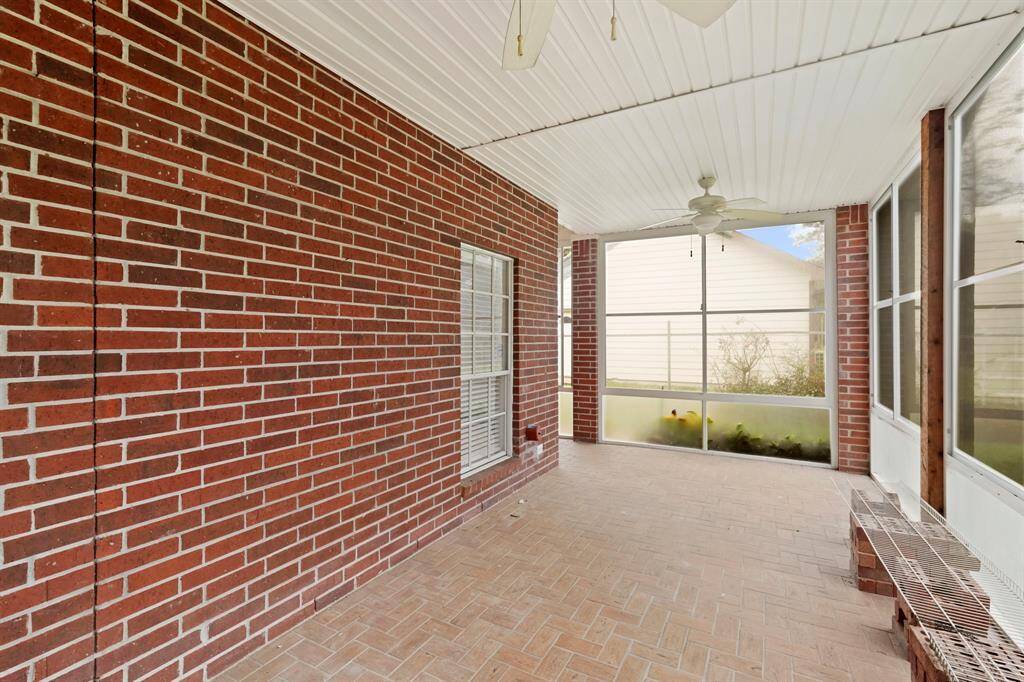 This screened-in porch area with brick walls and a tiled floor, featuring ceiling fans for comfort. It's an inviting space for relaxation or entertaining.