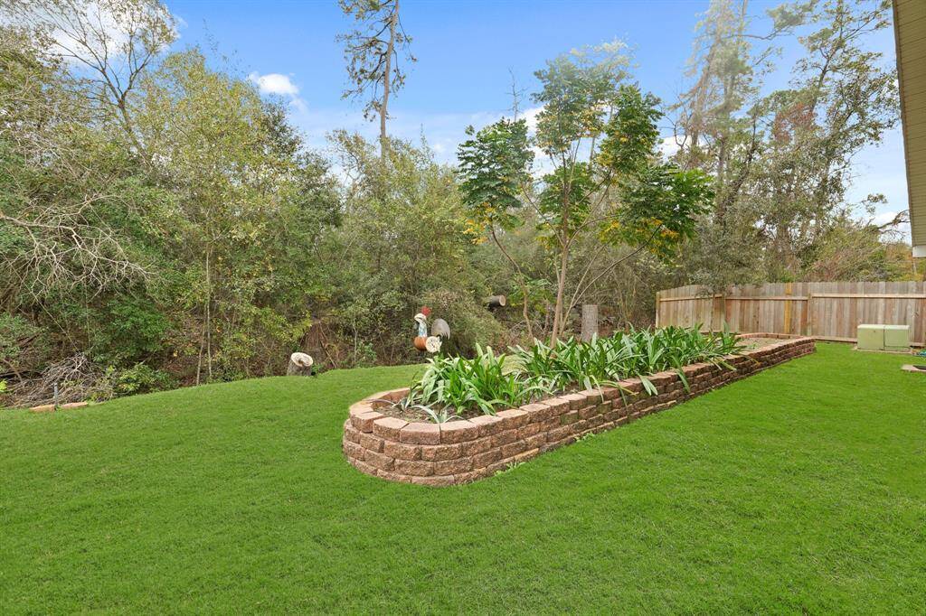 This photo showcases a spacious, lush backyard with a well-maintained lawn and a raised brick flower bed. It is bordered by a wooden fence and surrounded by mature trees, providing a private and serene outdoor space.