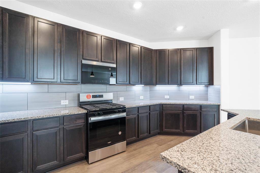 Another view of this beautiful kitchen showcasing the stainless steel Whirlpool gas range and microwave, and the granite countertop and modern tile backsplash.
