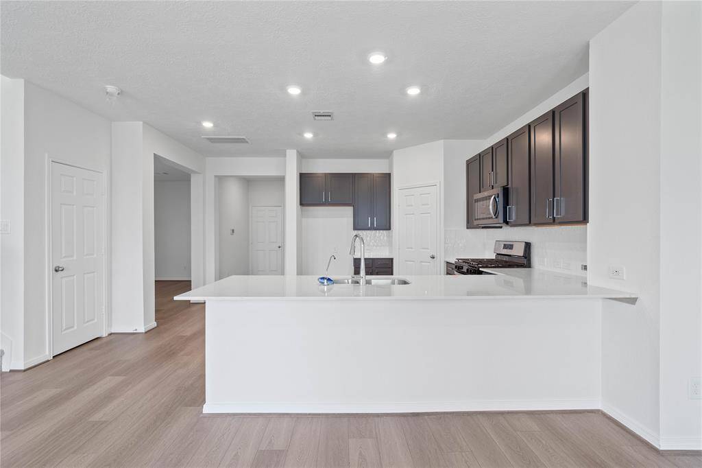 This spacious kitchen features high ceilings, stained wood cabinets, silestone countertops, SS appliances including microwave, modern tile backsplash, recessed lighting, extended countertop for breakfast bar, and a pantry all overlooking your huge family room.