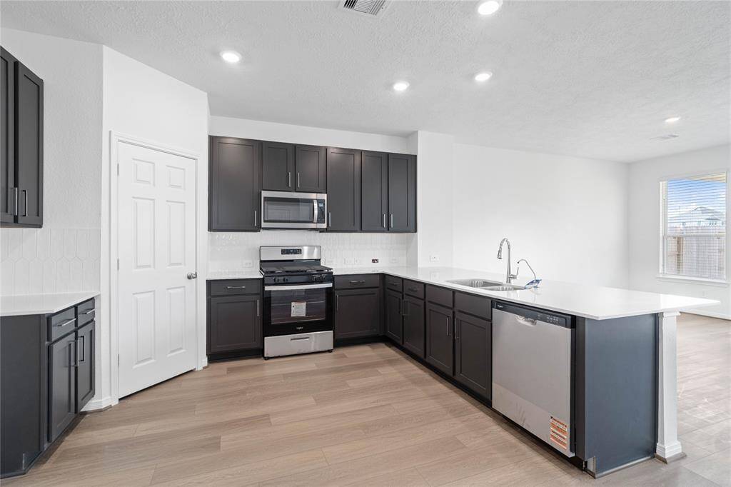 Another view of this spacious kitchen showcasing the gorgeous modern tile backsplash, SS appliances, Woodmont Dakota Shaker cabinets in Black Fox, and Silestone countertop in Lagoon.