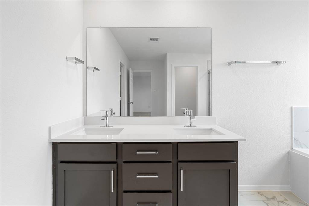This primary bathroom is definitely move-in ready! Pictured here is the spacious dual vanity area with stained cabinets and light countertops, high ceilings, neutral paint, sleek and modern finishes.