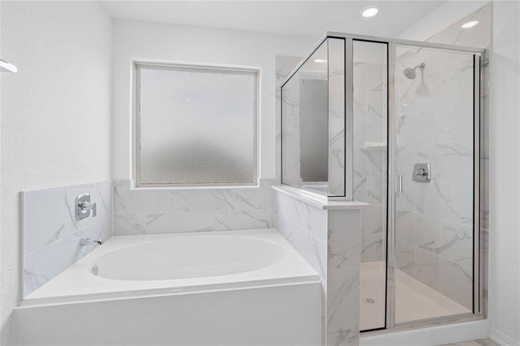 Another view of this primary bathroom features a walk-in shower with tile surround, garden tub, obscure window, neutral paint, and sleek and modern finishes.