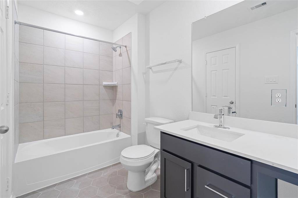 Secondary bath features tile flooring, bath/shower combo with tile surround, stained wood cabinets, beautiful light countertops, mirror, sleek fixtures and modern finishes.