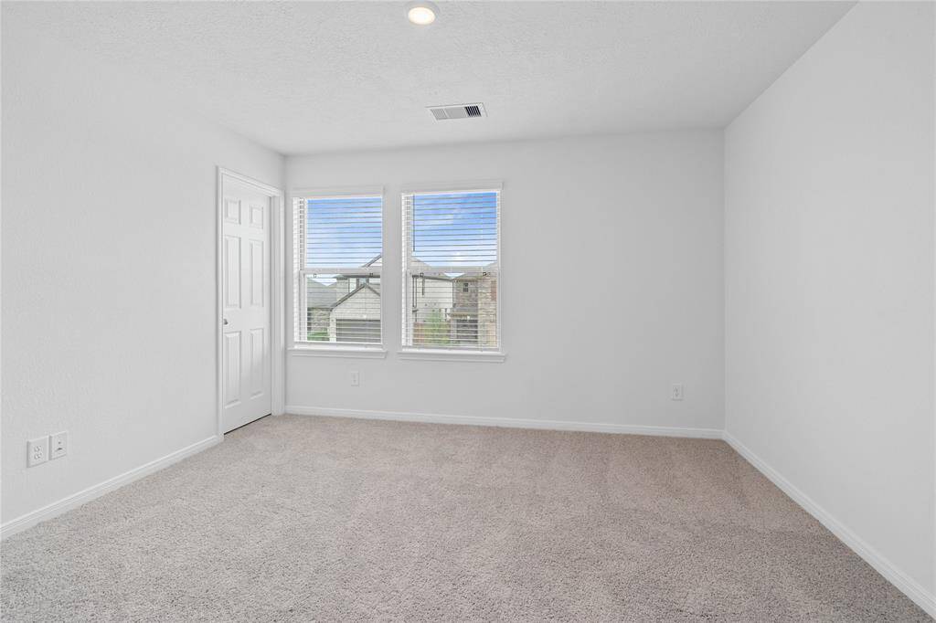 Secondary bedroom features plush carpet, neutral paint, recessed lighting, large window with privacy blinds and a walk-in closet.