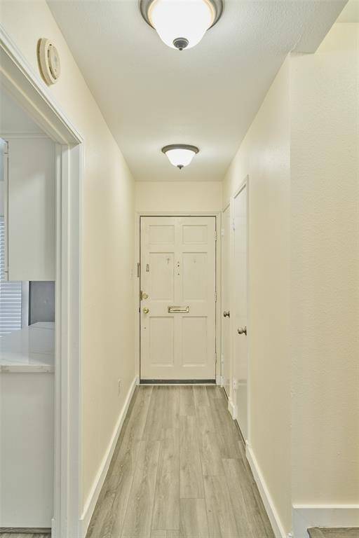 Bright and welcoming entryway with modern grey flooring, light walls, and stylish ceiling fixtures, leading to a secure main door with a peephole and deadbolt.