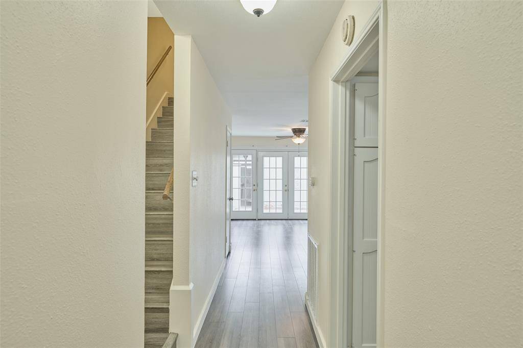 This bright entryway features sleek hardwood floors, a left-side staircase, and opens to a sunlit room through French doors, perfectly blending modern style and warmth.