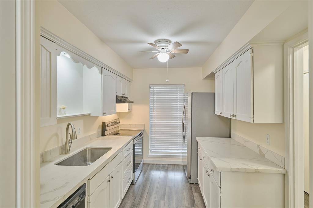 Bright and modern kitchen with white cabinetry, stainless steel appliances, marble-style countertops, and wood flooring. Enjoy comfort with a ceiling fan and direct access to a sunlit room through sliding doors.