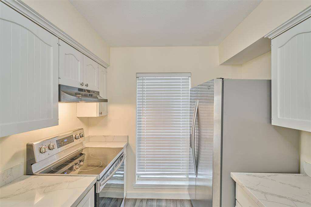 Experience modern living in this bright kitchen featuring sleek white cabinetry, marble-effect countertops, and stainless steel appliances, all enhanced by a wood-look floor.