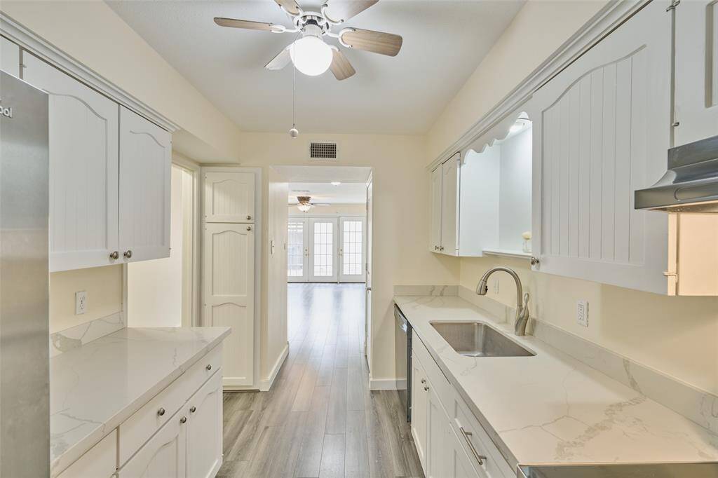 Discover a bright, modern kitchen with sleek white cabinetry, elegant marble countertops, stainless steel appliances, and warm wood flooring, seamlessly connecting to the living area.