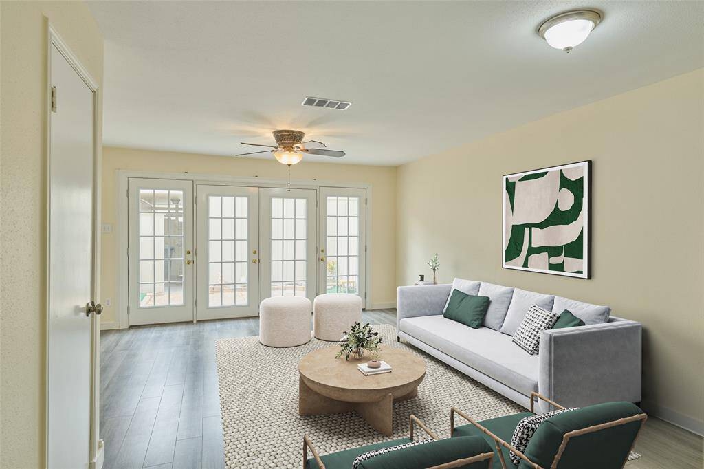 This bright, contemporary living room features large French doors for abundant natural light, a cozy seating area with green accents, and stylish gray flooring.This photo is virtually staged.