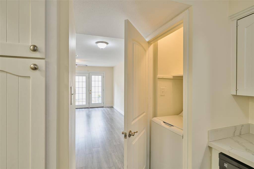 Discover a bright hallway leading to a sunlit room through elegant French doors. Enjoy the convenience of a laundry nook with modern cabinetry and a sleek marble-like countertop. The space features stylish wood-look laminate flooring throughout.