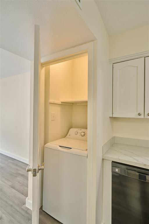Discover a tidy, compact laundry closet with a washer, conveniently located off a kitchen featuring modern cabinetry and updated appliances. Enjoy the clean, neutral tones and stylish wood-look flooring.