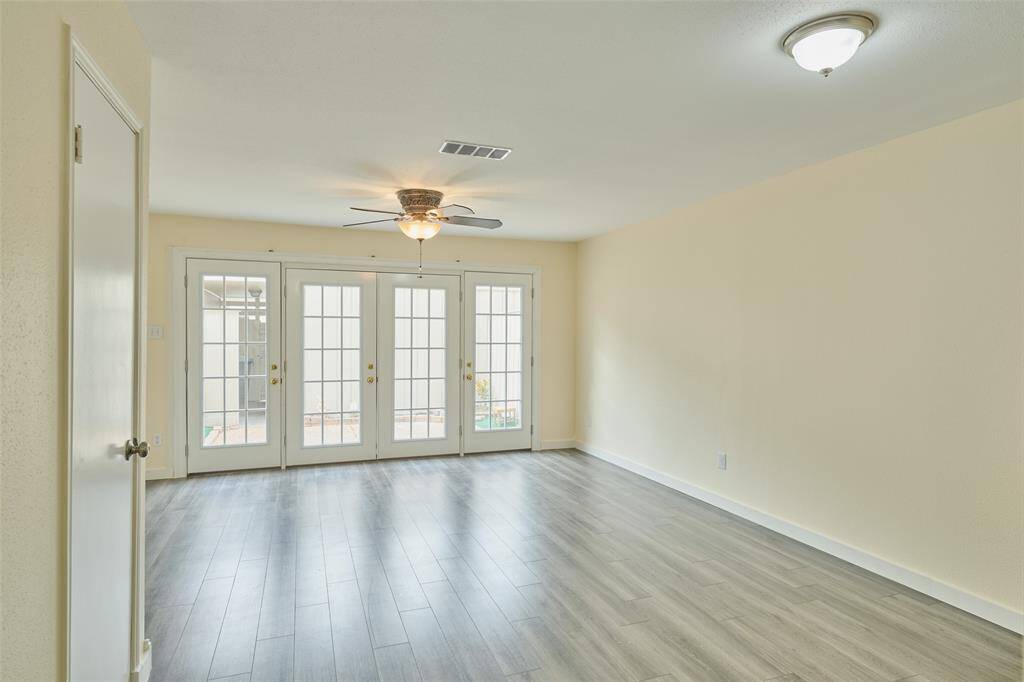 Bright and spacious room with modern grey flooring, a ceiling fan, and abundant natural light from French doors opening to the outside.