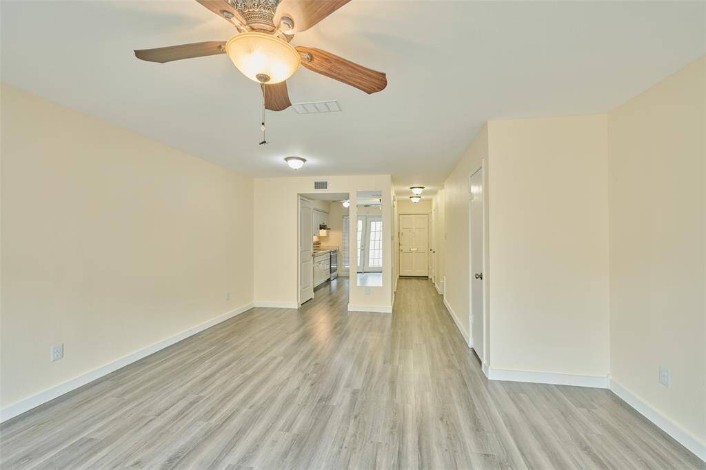 Experience a bright, open-concept space with stylish wood-look flooring, neutral tones, and a ceiling fan. The practical layout includes a hallway leading to additional rooms.