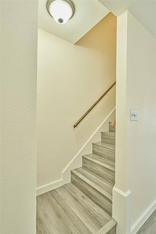 Bright and inviting staircase featuring modern gray flooring and a sleek wooden handrail, leading to the home's upper level. The neutral-toned walls enhance its clean, contemporary appeal.