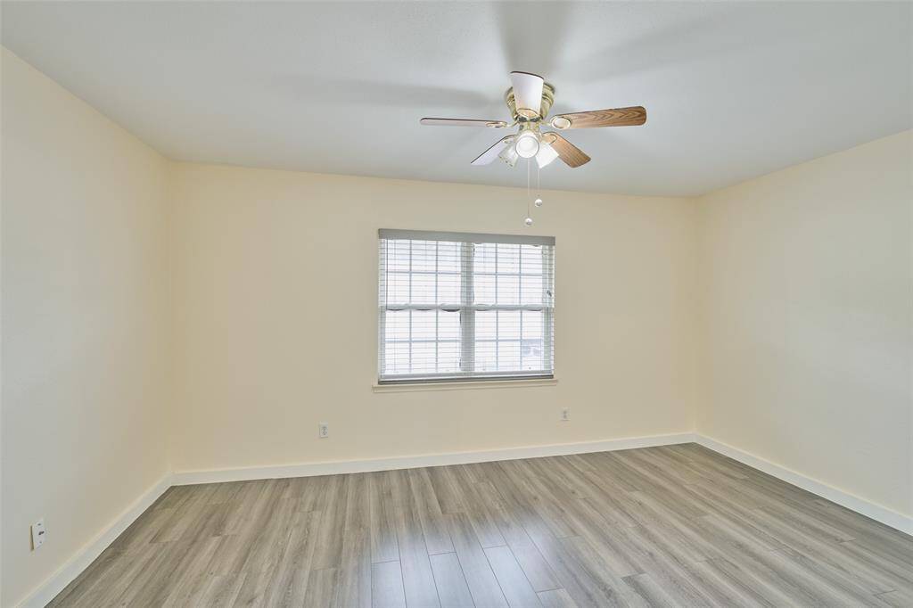Bright room with modern gray laminate flooring, neutral walls, and a ceiling fan. A single window floods the space with natural light.