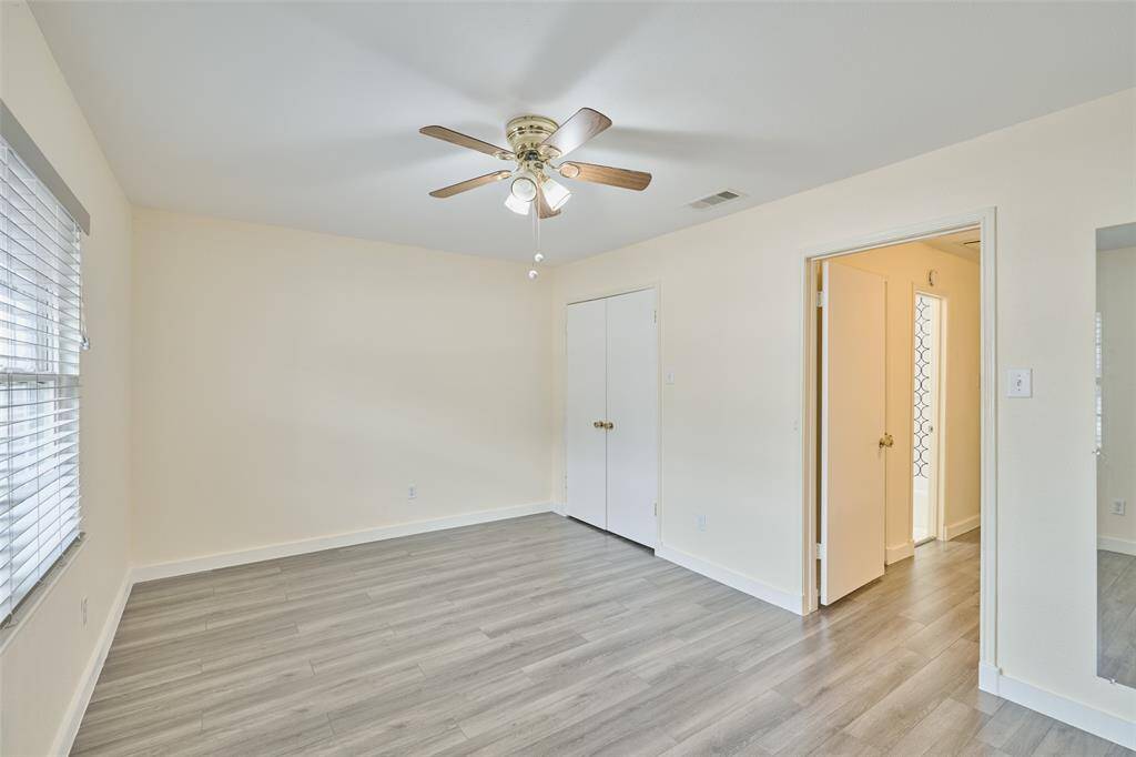 Bright and airy room with fresh neutral paint, contemporary gray laminate flooring, and a ceiling fan. Features a large window for natural light and two doorways connecting to the home.