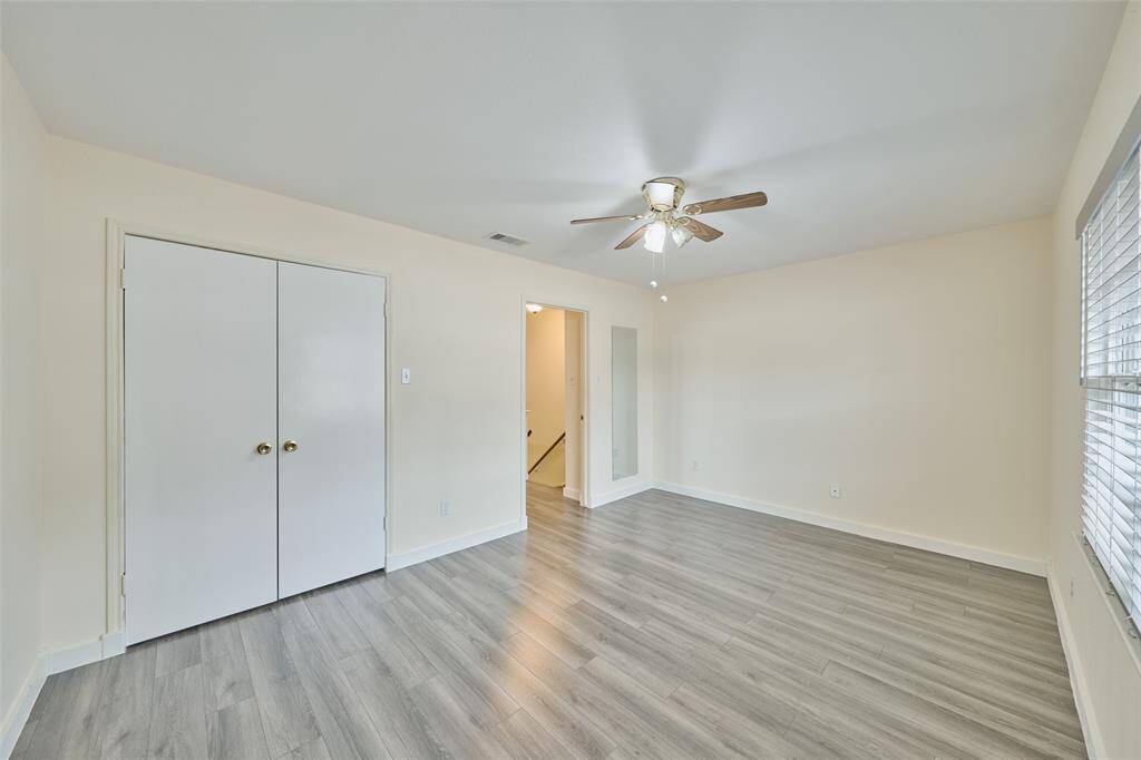 This bright room features light wood flooring, a ceiling fan, and ample natural light from large windows. It includes a double-door closet and offers a neutral palette, ideal for personalization.