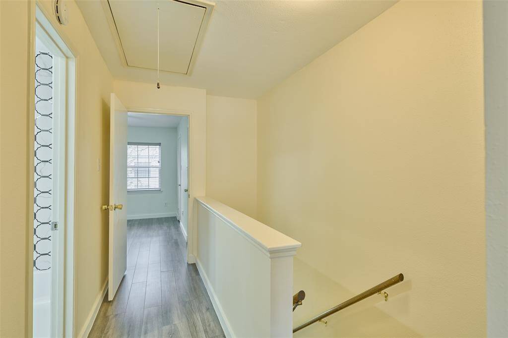 Step into a bright hallway featuring sleek wood-look flooring, a stylish glass-paneled door, and a modern half-wall with a wooden handrail. A welcoming, well-lit room awaits ahead.