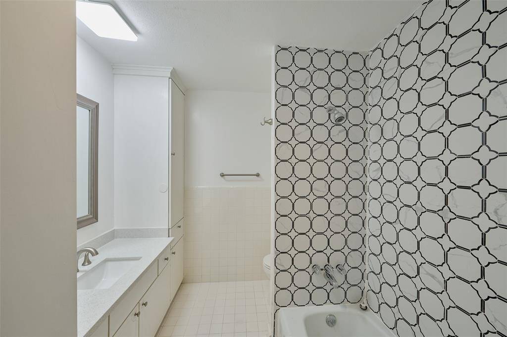 Explore this pristine bathroom featuring a spacious single vanity, a large mirror, and a stylish tub-shower with striking black and white tiles.