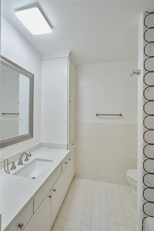 This bright and pristine bathroom boasts a large mirror, spacious single vanity with white cabinetry, a walk-in shower with safety grab bars, and a separate toilet area.