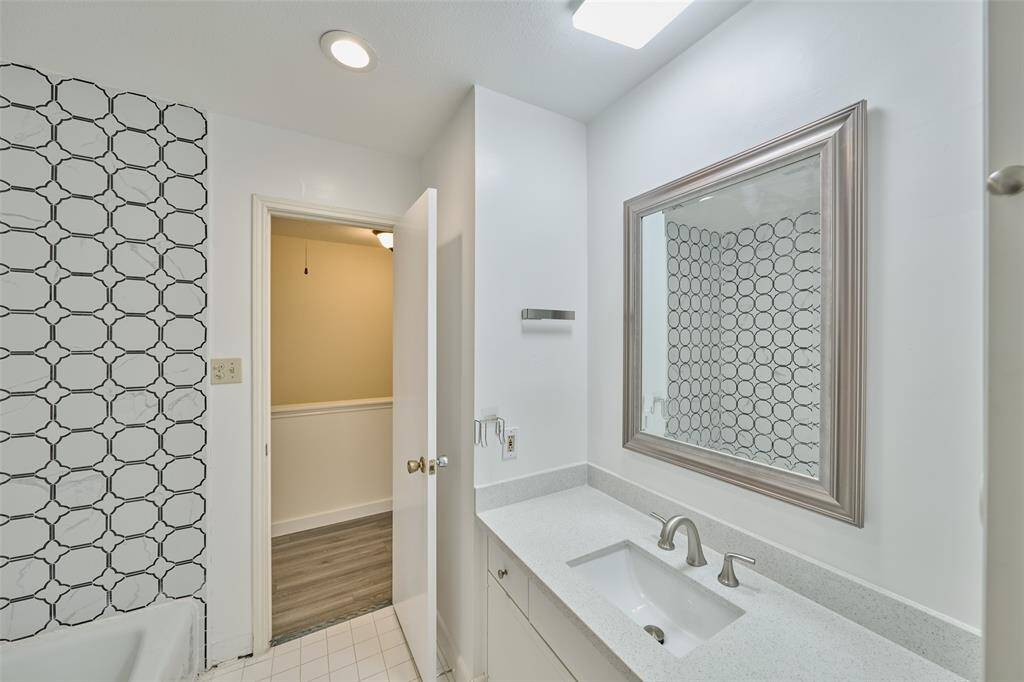 This bathroom features a modern design with a large mirror, sleek countertop, and stylish geometric tile accent wall. The space is bright with recessed lighting and has a clean, contemporary feel.