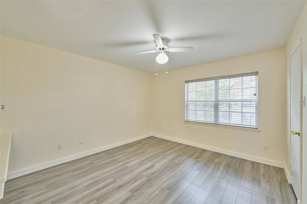 Bright room with modern grey laminate flooring, neutral walls, and a large window with blinds. Features a ceiling fan with light.