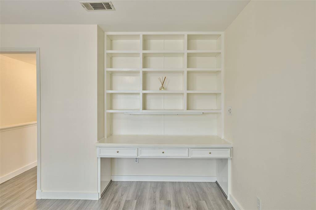This room boasts a sleek built-in white desk with shelving, set against neutral walls and modern grey flooring—perfect for a home office or study.