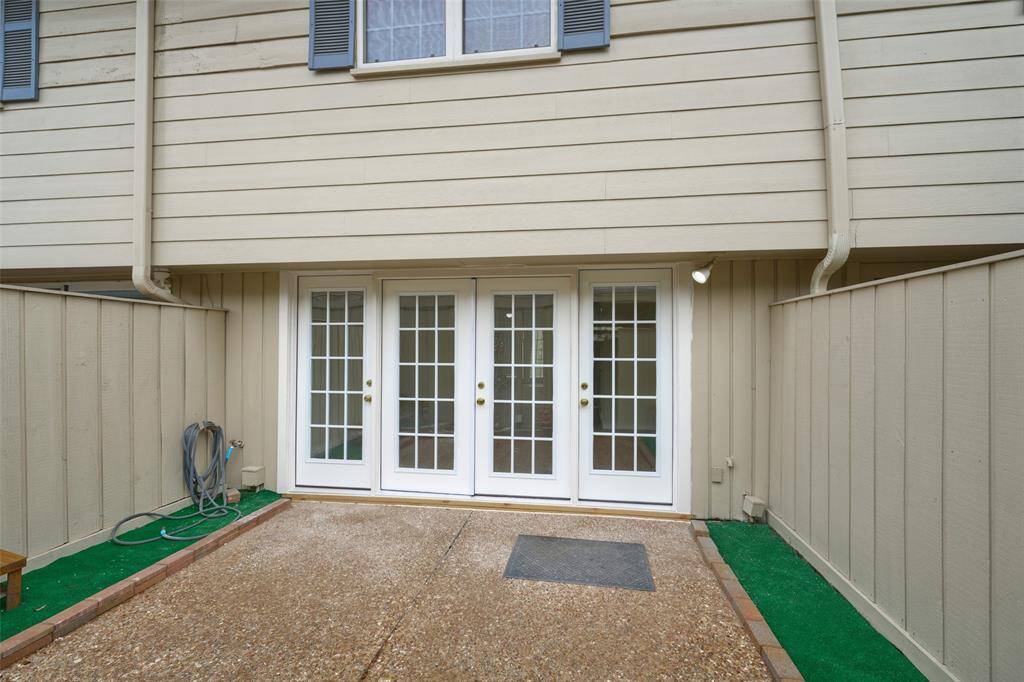This inviting ground-level patio features elegant double French doors, a neat concrete area, and a touch of artificial turf. Enclosed by beige siding, it's perfect for personalizing with outdoor furniture or plants.