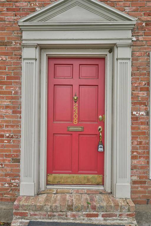 Charming red door set in a classic brick facade, accented by elegant white trim. A small step enhances the welcoming entrance.