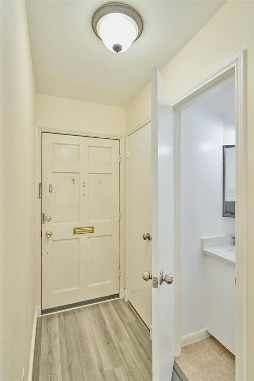 Bright and inviting entryway with stylish wood-look flooring, a welcoming front door with mail slot, and a view into a modern, well-lit bathroom.