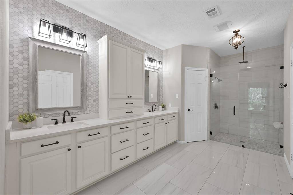 The spa-inspired primary bath features dual vanities, designer lighting, and an oversized glass-enclosed shower—blending luxury and functionality in a space designed to unwind.