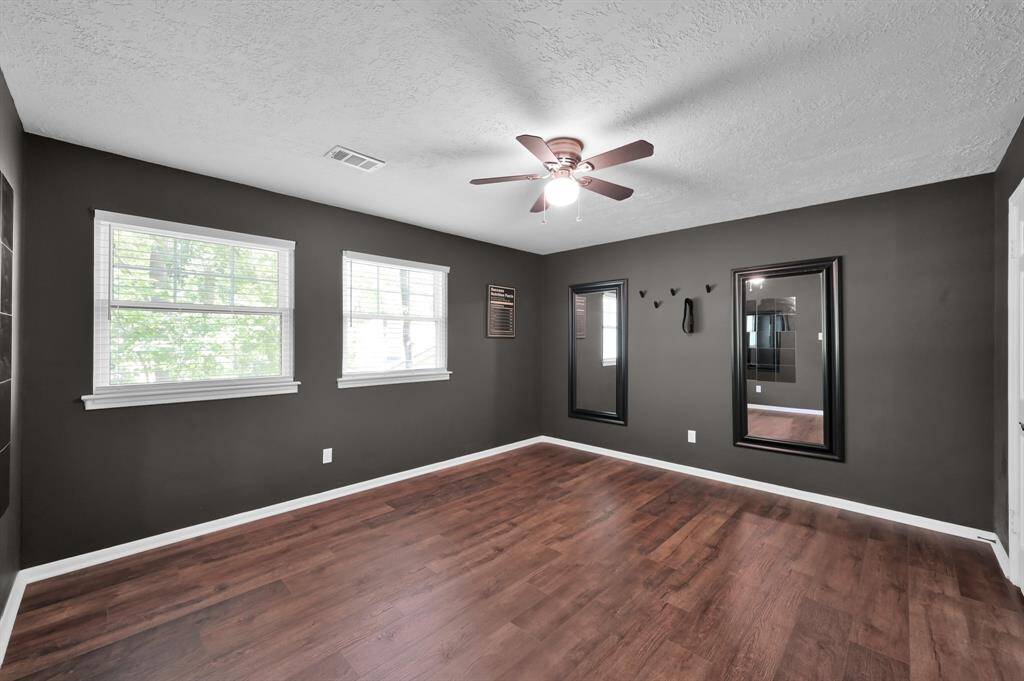 This stylish secondary bedroom features bold wall color, rich flooring, and multiple windows for natural light—perfect as a guest suite, teen retreat, or creative studio space.