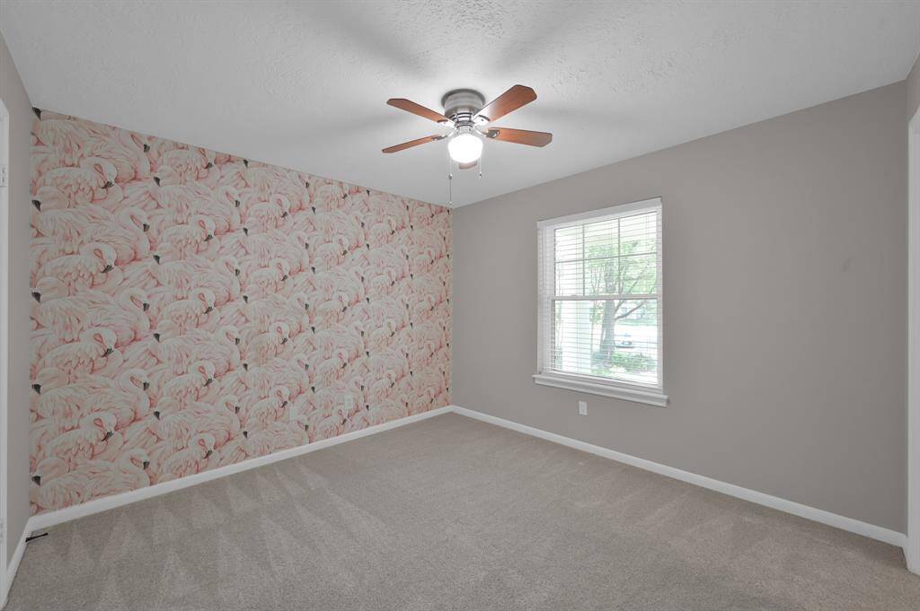 This charming secondary bedroom features soft neutral tones, plush carpeting, and a playful accent wall—perfect for a nursery, guest space, or creative retreat.