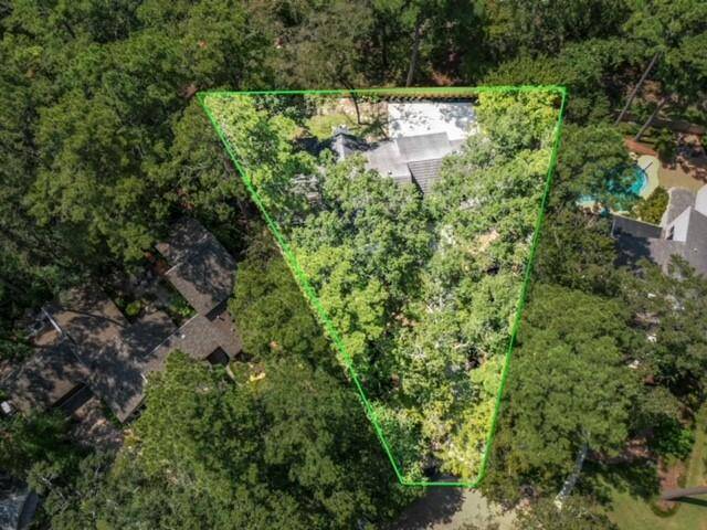 This aerial photo shows a triangular wooded property, outlined in green, featuring the house partially visible through the trees. The home is surrounded by lush greenery, offering privacy and a serene, natural setting.