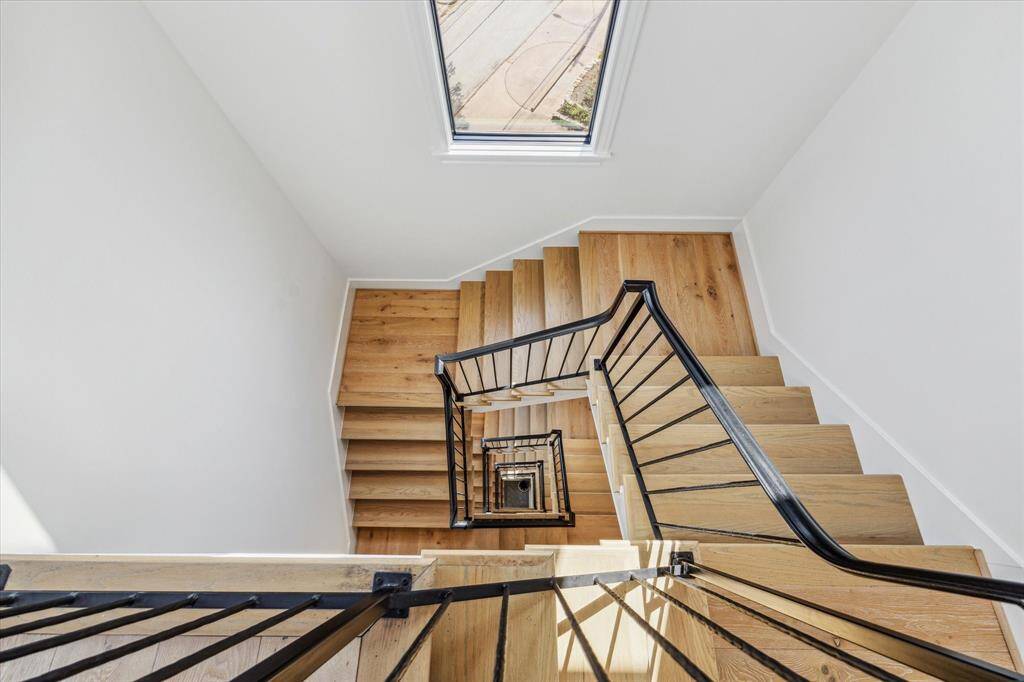 An elegant staircase with wood planks and a wrought iron railing extends all five floors.
