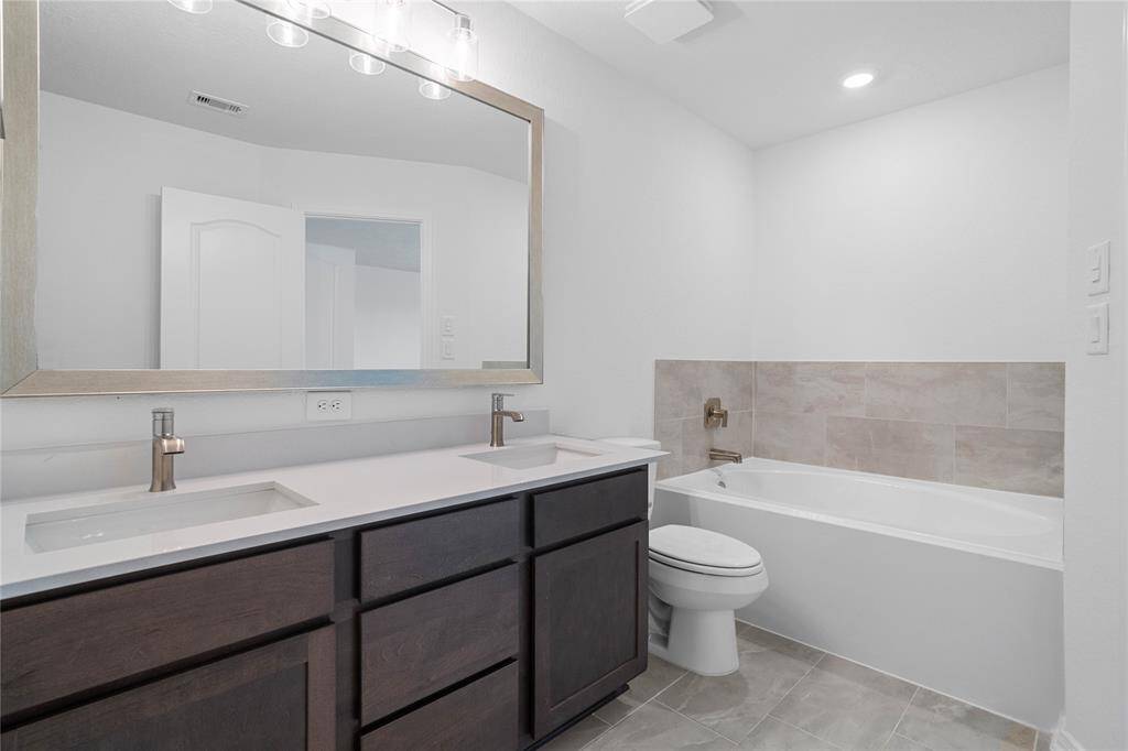 This primary bathroom is definitely move-in ready! Featuring an oversized tub with tile surround, stained cabinets with light countertops and dual vanities, framed mirror, high ceilings, custom paint, sleek and dark modern finishes.