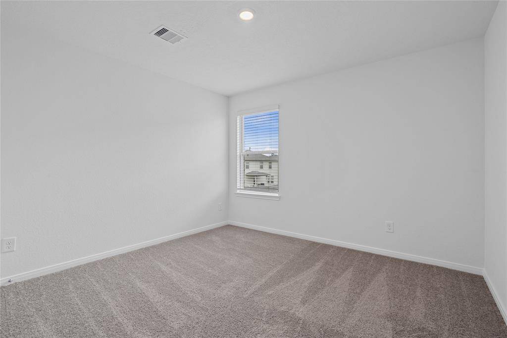 Secondary bedroom features plush carpet, custom paint, closet space, and a large window with privacy blinds.