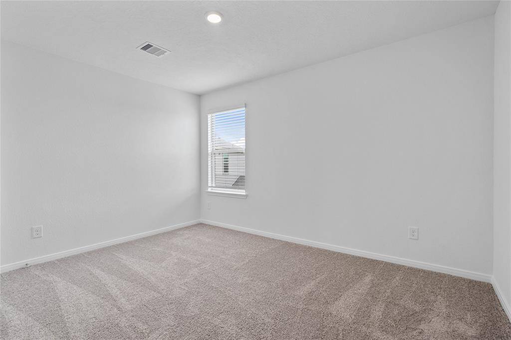 Secondary bedroom features plush carpet, custom paint, closet space, and a large window with privacy blinds.
