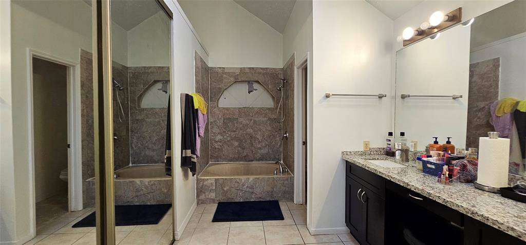 Oval tub a shower-tub combo with marble-like tile and larrge walk in closet.